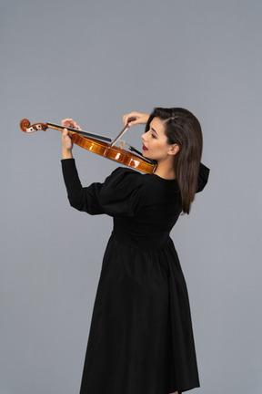 Close-up de uma jovem alegre de vestido preto tocando violino