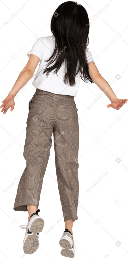 Vista posteriore di una giovane donna che salta in calzoni e t-shirt allargando le mani