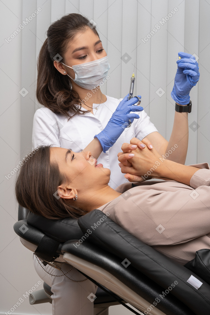 A female dentist holding syringe and a  scared female patient holding hands together