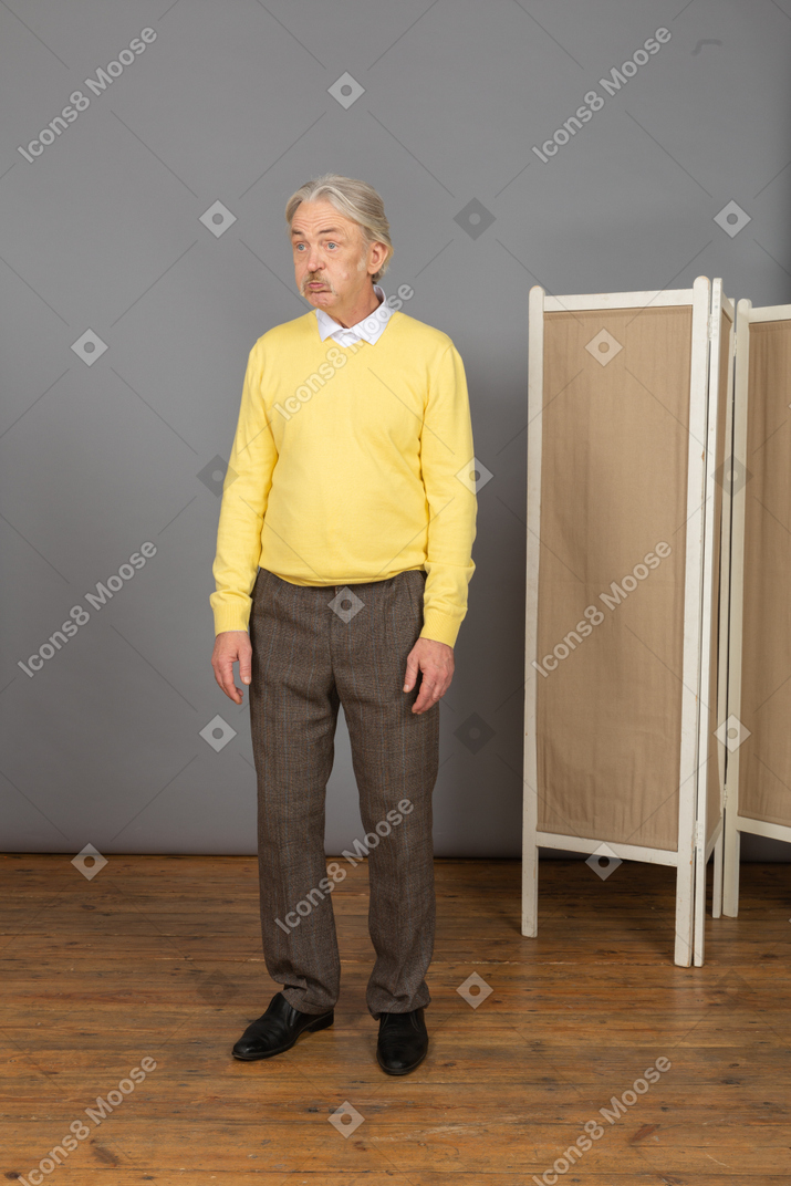 Vista de tres cuartos de un anciano decepcionado soplando mejillas