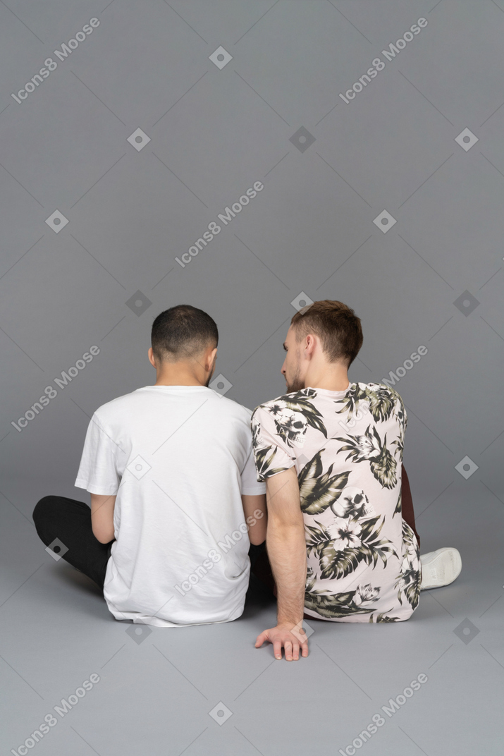 Vue arrière de deux jeunes hommes assis sur le sol
