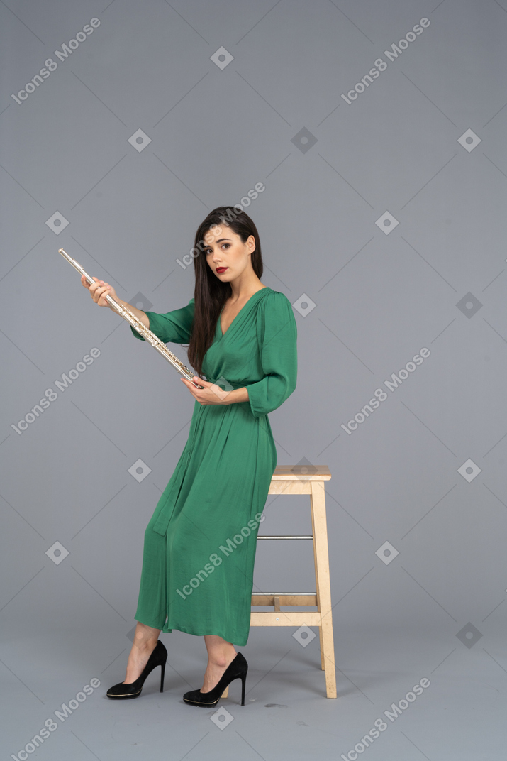 Side view of a young lady in green dress sitting on a chair and holding clarinet