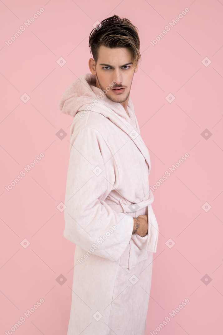 Красивый парень в розовом халате стоит с руками в карманах