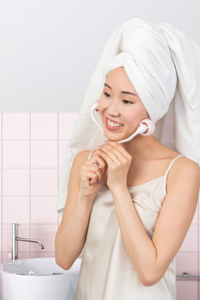 A woman with a towel on her head using a face massager