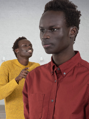 A man looking away from camera standing next to a man with closed eyes