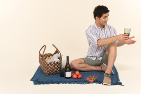 Jovem homem caucasiano segurando o copo de vinho enquanto está sentado no cobertor