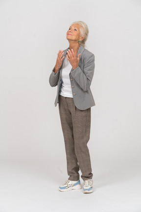 Vista lateral de una anciana feliz en traje mirando hacia arriba y rezando