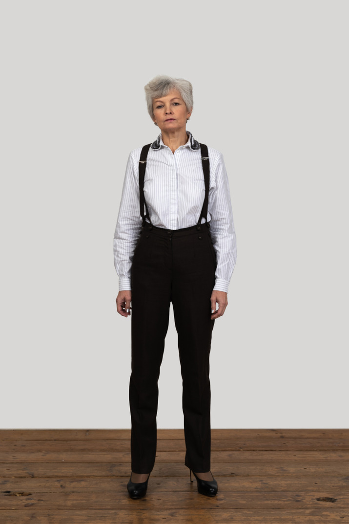 Front view of a serious old female in office clothes standing still in the room