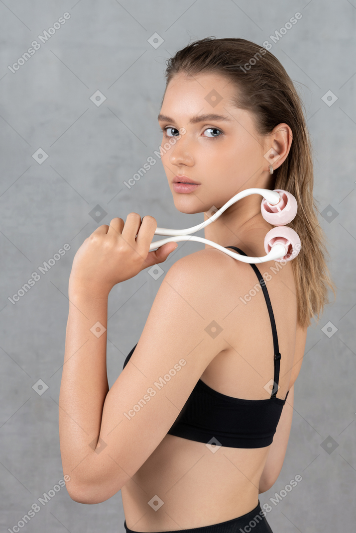 Side view of a young woman looking at camera with face roller in hand