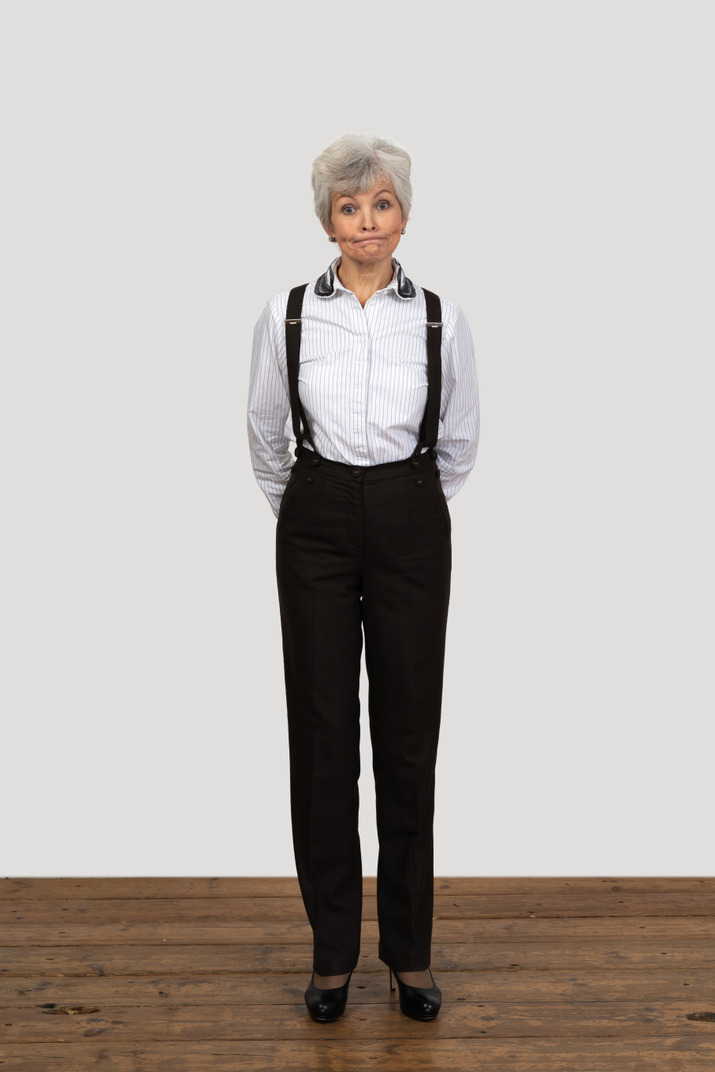 Front view of an old displeased female in office clothes grimacing with her hands behind back