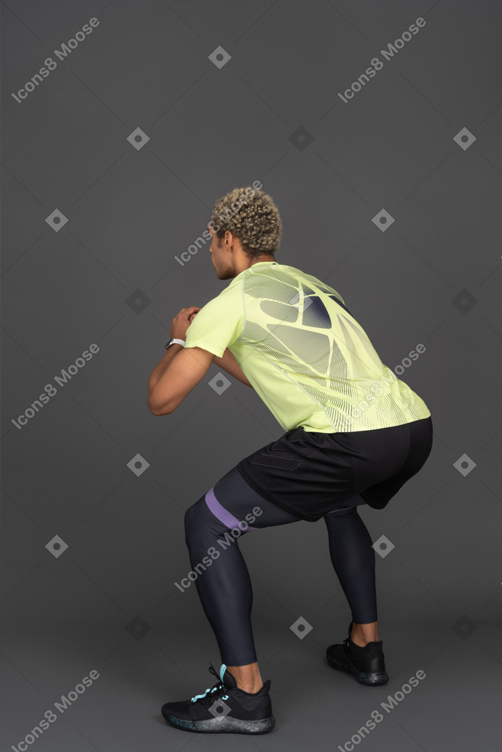 Three-quarter back view of a dark-skinned young man squatting with an elastic rubber
