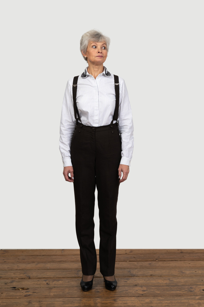 Front view of an old curious female in office clothes standing still indoors looking aside