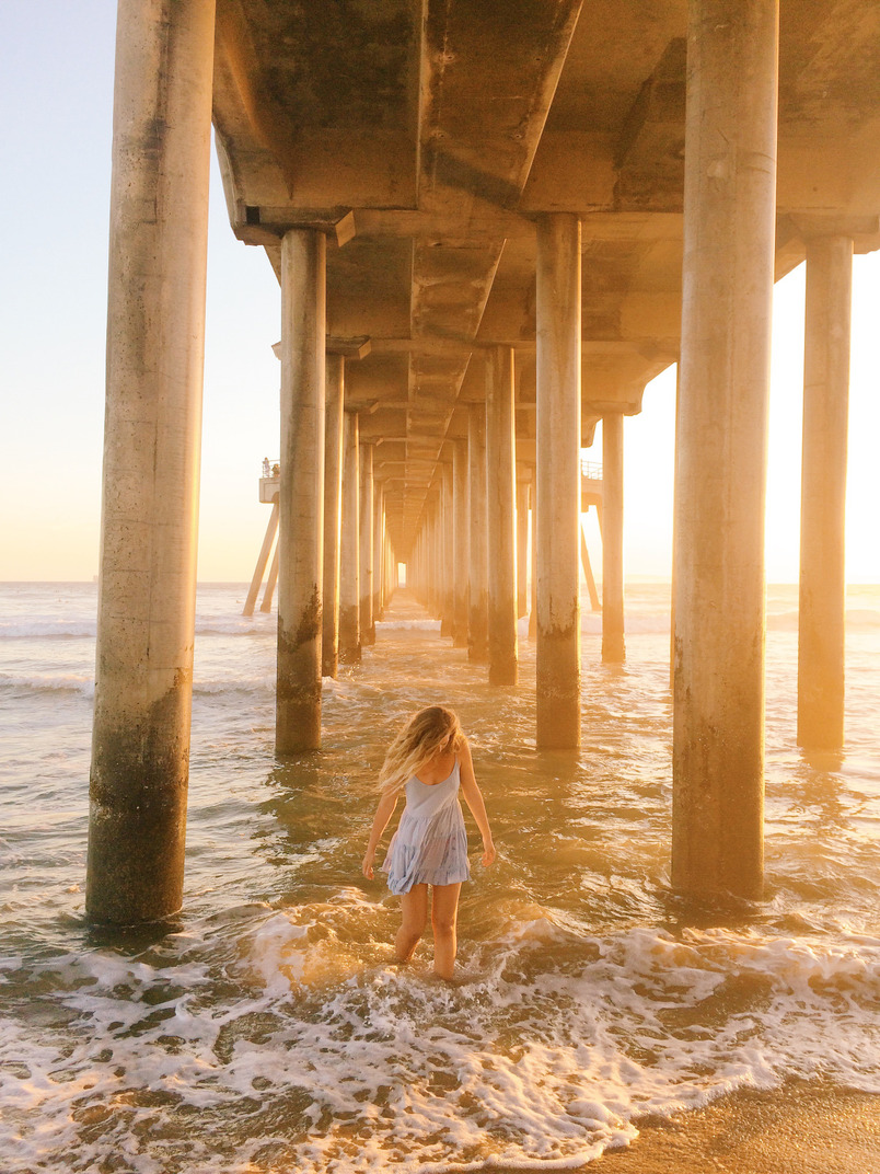 Молодая женщина в платье стоит по колено в океане