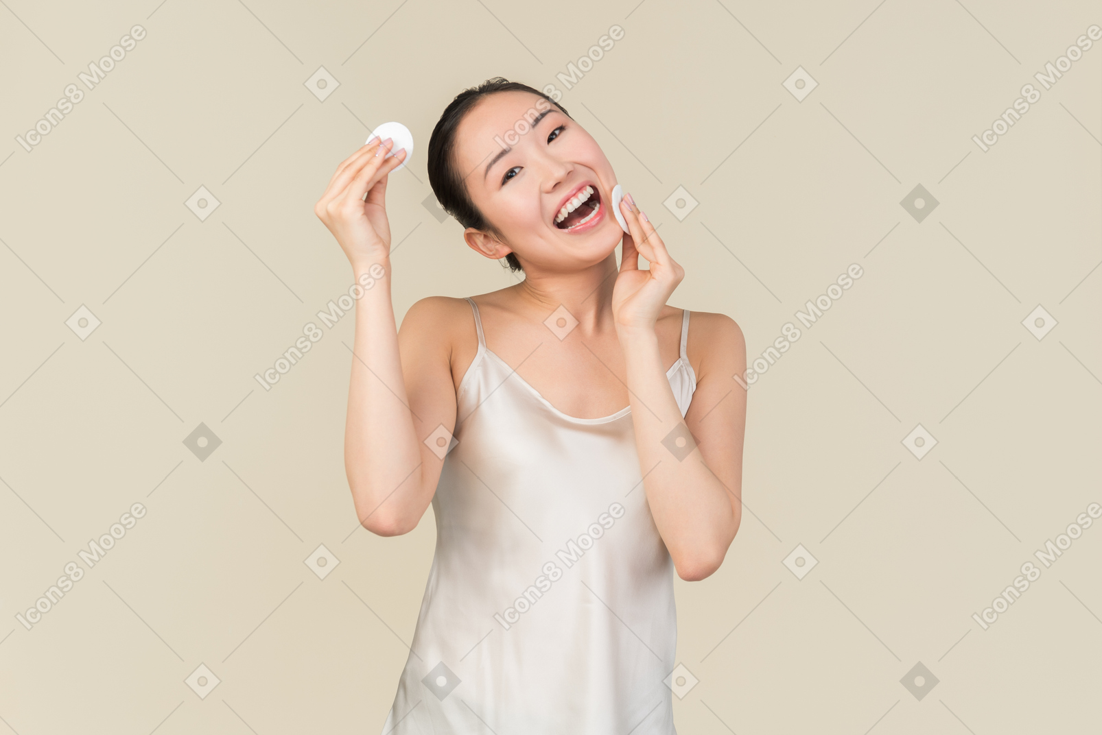 Laughing asian girl cleaning her face with cotton pads