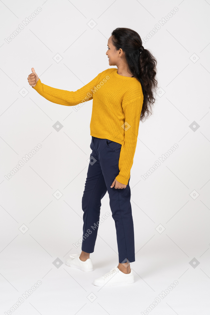 Side view of a happy girl in casual clothes showing thumb up and looking aside