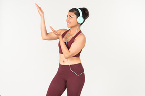 Улыбающаяся молодая индийская женщина в спортивном костюме, слушающая музыку в наушниках