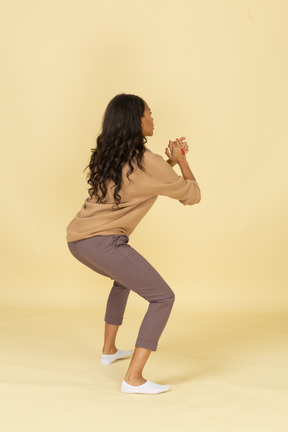 Three-quarter back view of a squatting dark-skinned young female with her legs widespread