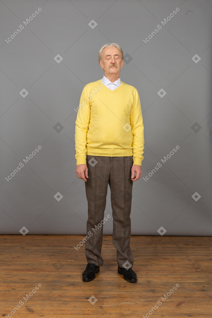 Front view of an old man wearing yellow pullover and standing still with his eyes closed