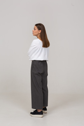 Vista posterior de tres cuartos de una joven en ropa de oficina cruzando los brazos