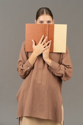 Woman covering face with a book and looking at camera