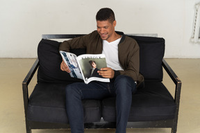 Beautiful young man sitting on a sofa and holding a magazine