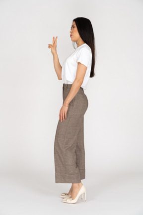 Side view of a young woman in breeches showing peace sign