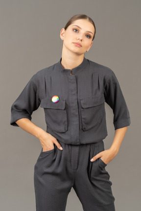 Front view of a young woman in a jumpsuit with lgbt pin putting hands in pockets