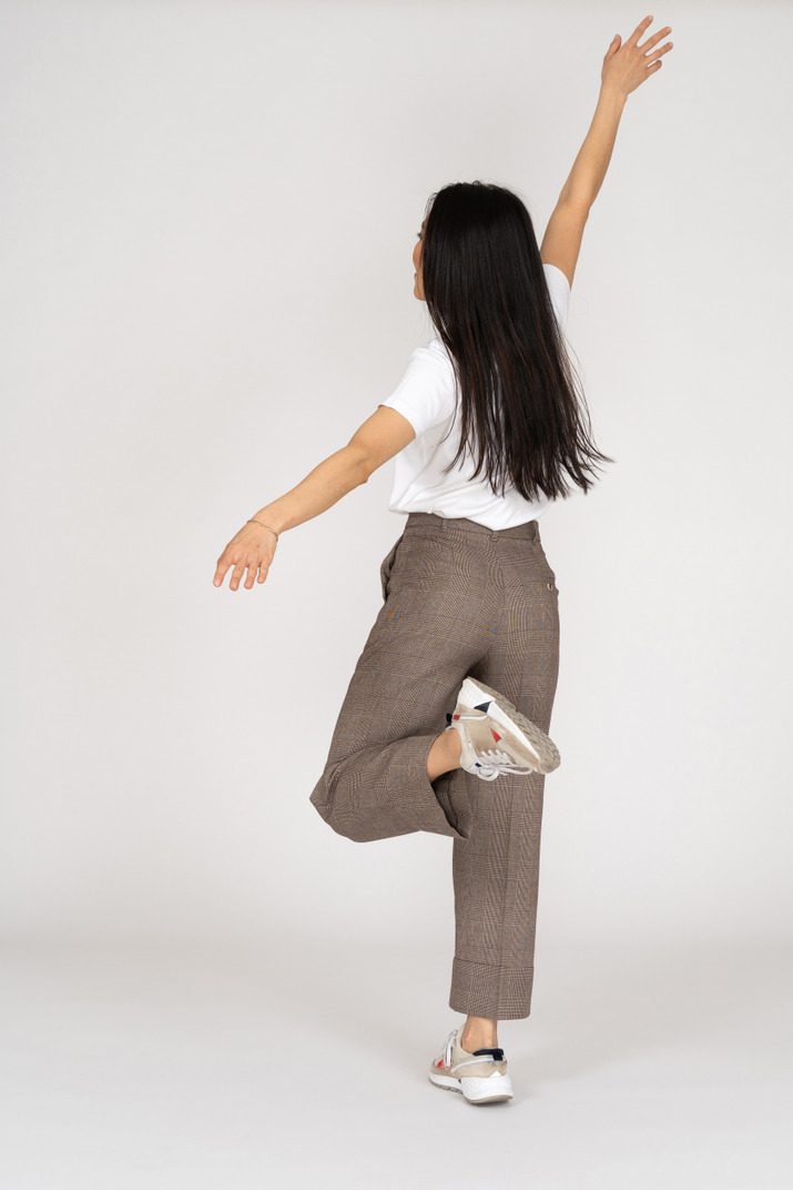 Back view of a dancing young lady in breeches and t-shirt outstretching her hand