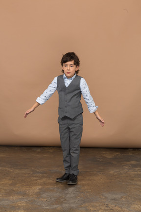 Front view of a cute boy in suit standing with outstretched arms