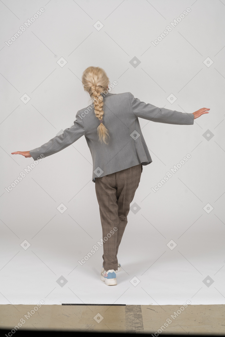 Rückansicht einer alten dame im anzug, die mit ausgestreckten armen posiert
