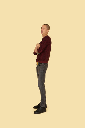 Side view of a displeased young man dressed in casual clothes crossing his hands