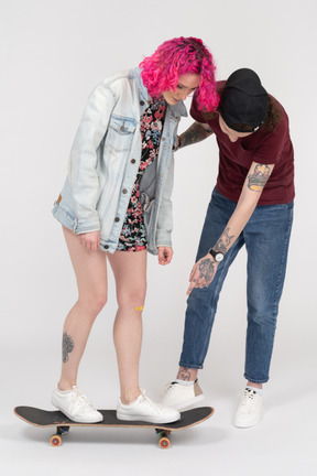 Boy teaching a teenage girl to ride a skateboard