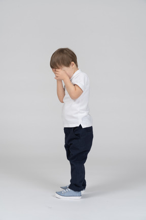 Side view of little boy covering his face with his hands