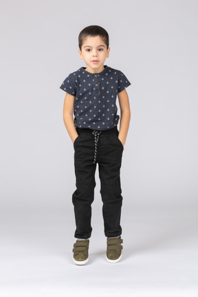 Вид спереди симпатичного мальчика в повседневной одежде, позирующего с руками в карманах и смотрящего в камеру