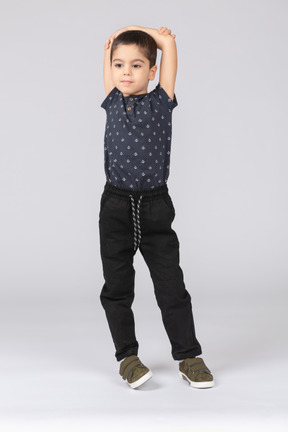 Vista frontal de un chico lindo de pie con las manos por encima de la cabeza y mirando a la cámara
