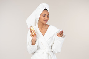 Black woman in white bathrobe and head towel enjoying her skin care routine