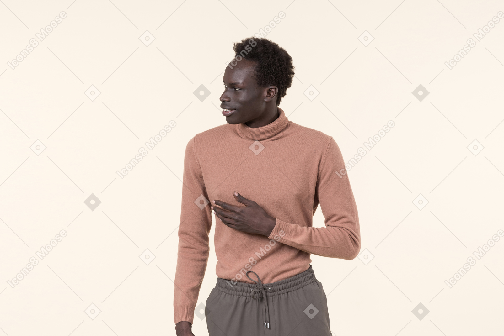 Um jovem negro em uma gola alta bege e calça de moletom cinza em pé casualmente sobre o fundo branco