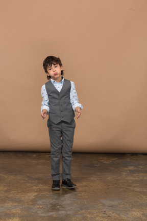 Vista frontal de um menino bonito de terno cinza fazendo caretas e gesticulando