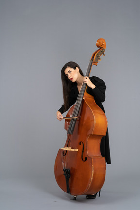 Three-quarter view of a young woman in black dress playing the double-bass with a bow