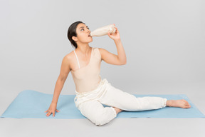 Jeune femme indienne assise sur un tapis de yoga et de l'eau potable