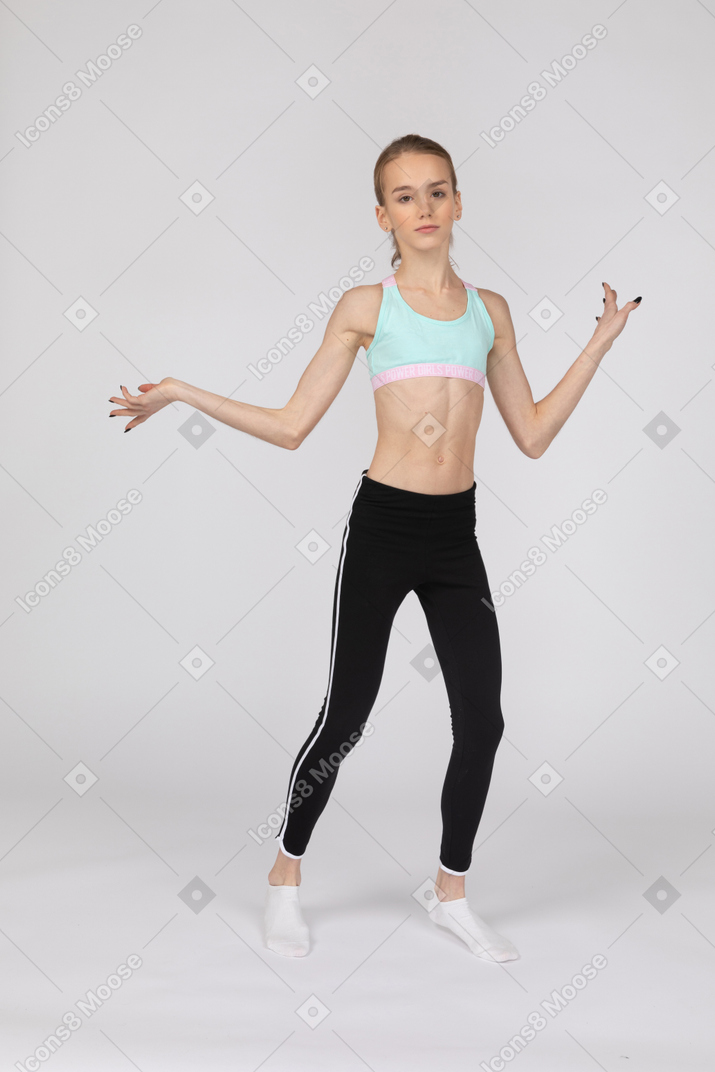 Vista frontal de una jovencita en ropa deportiva levantando las manos y bailando