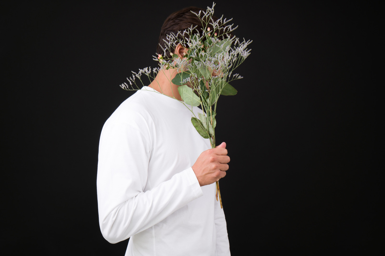 Shy young man hiding his face in a bunch of flowers