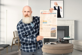 A bald man holding up a newspaper in a living room