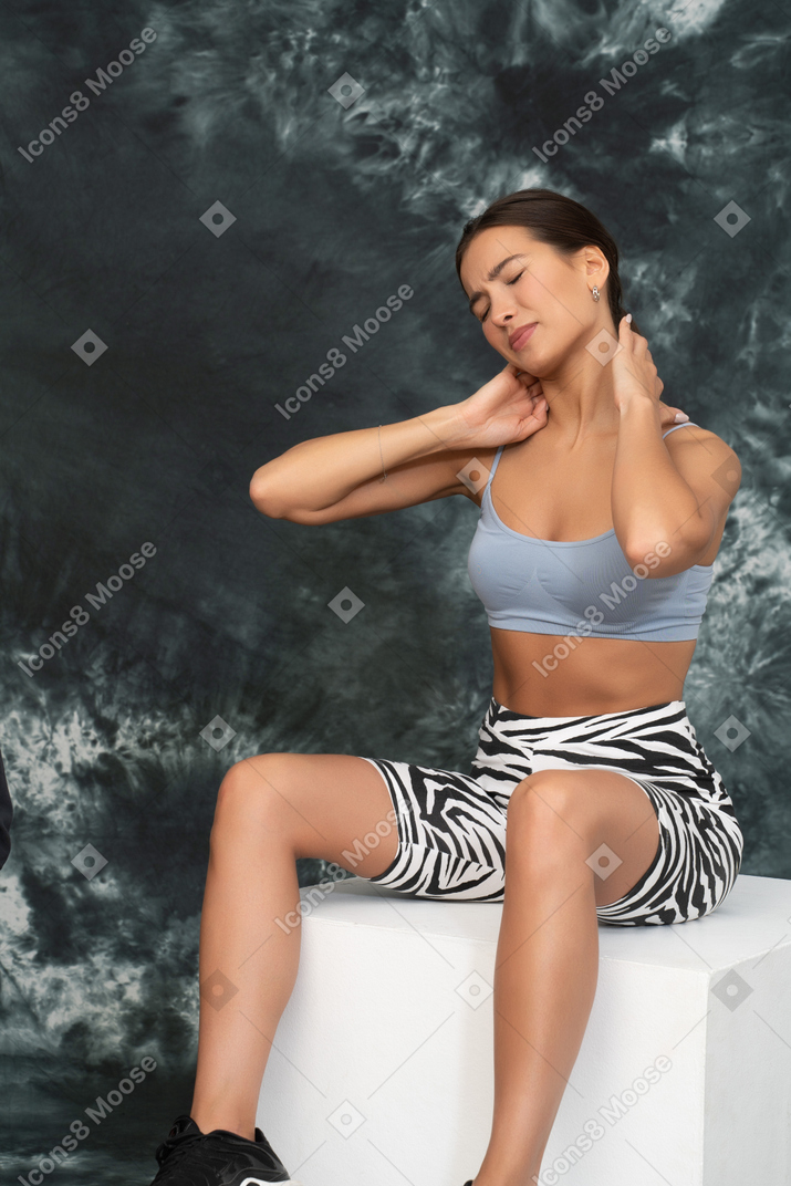 Young woman in sports clothes feeling pain in her neck