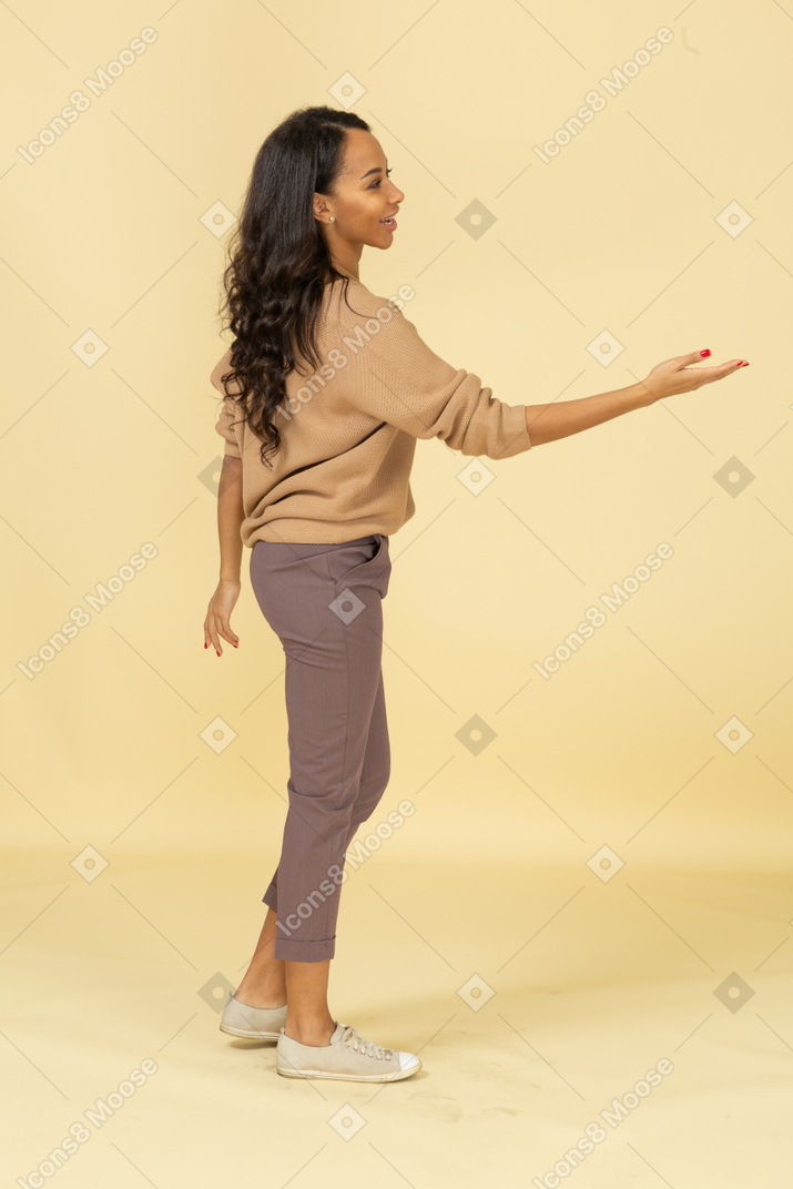 Vista lateral de uma jovem mulher de pele escura estendendo a mão