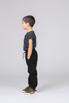 Вид сбоку на мальчика в повседневной одежде, стоящего с руками в карманах