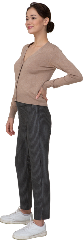 Vista di tre quarti di una femmina soddisfatta in pullover e pantaloni che mette la mano sull'anca