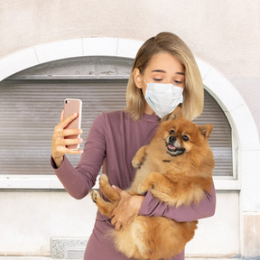 Woman in face mask taking selfie with dog