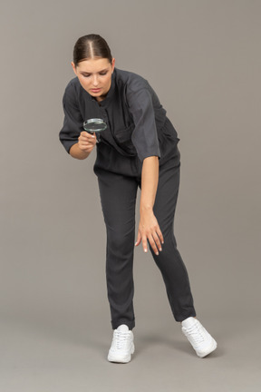 Front view of a young woman in a jumpsuit holding a magnifying glass