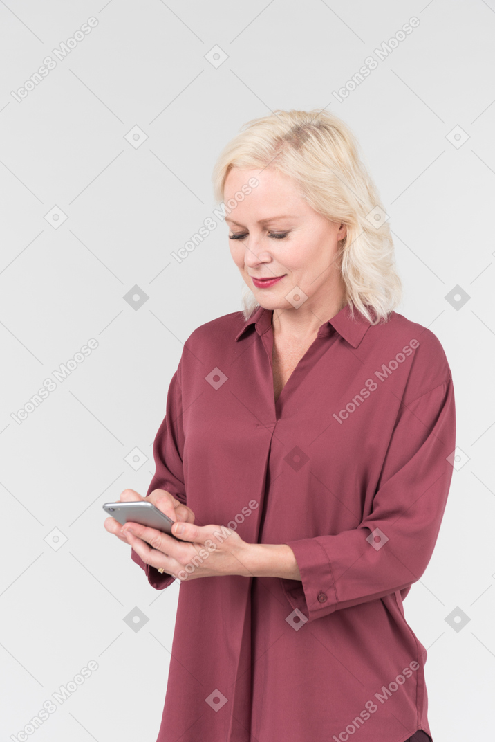 A nice-looking middle-aged blonde woman in a burgundy shirt and with a smartphone in her hand